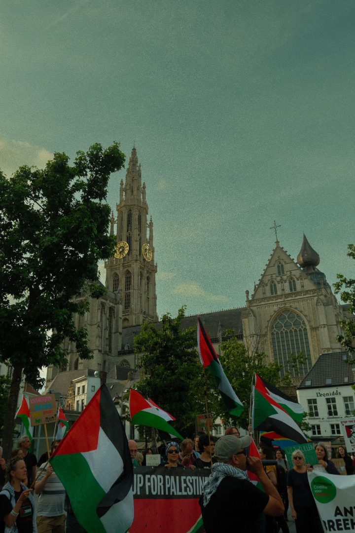 De afbeelding is een verticale foto van de pro Palestijnse protesten met de kathedraal van Antwerpen op de achtergrond.